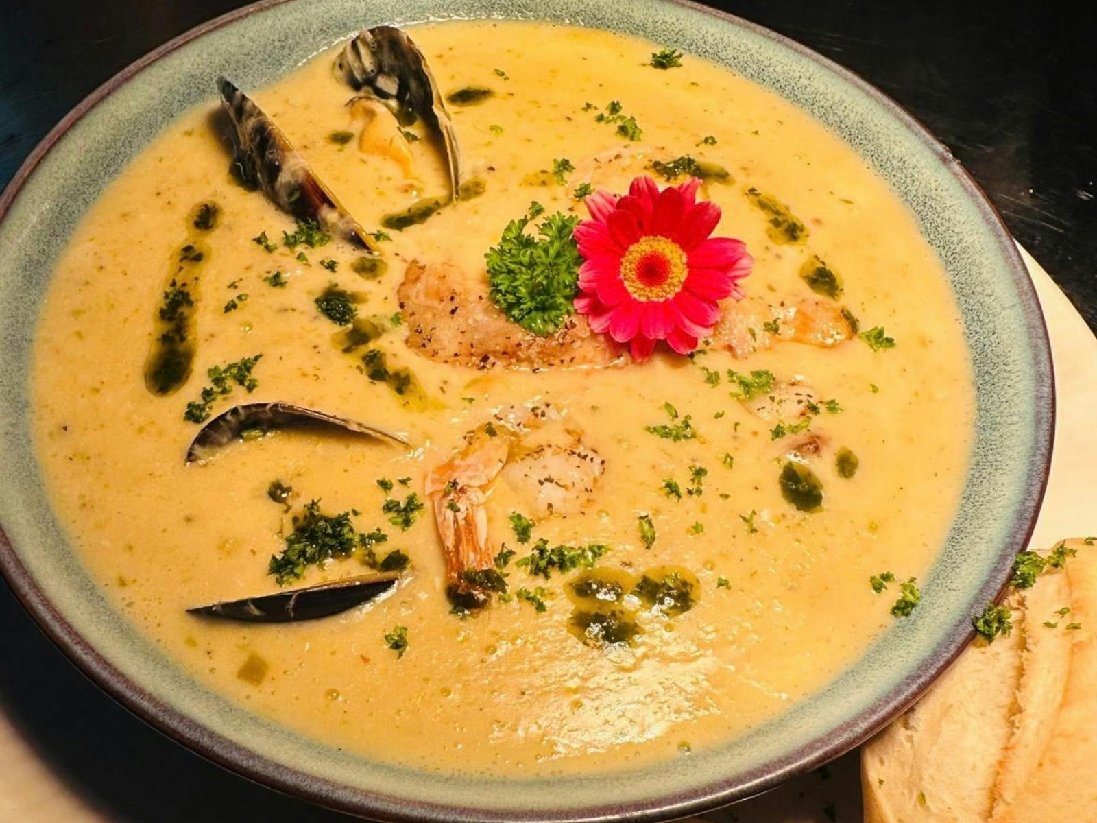 Creamy seafood chowder with fish, prawns and mussels, finished with herbs and served with bread at T