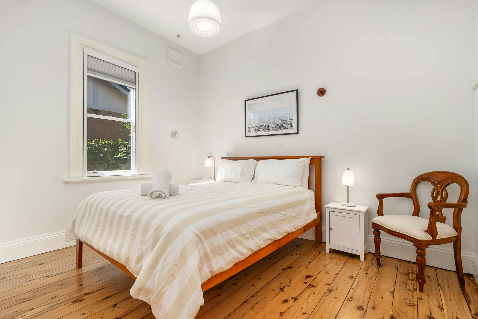 Bedroom with queen bed, window allowing sunlight and wooden furniture