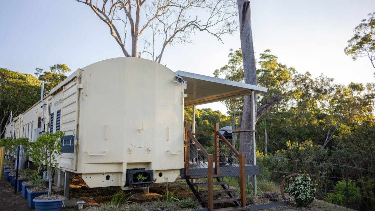 Restored train carriage accommodation with a private deck, set among lush greenery at Hitching Rail
