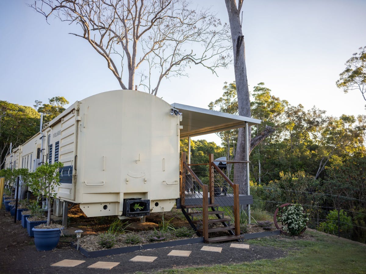 Restored train carriage accommodation with a private deck, set among lush greenery at Hitching Rail