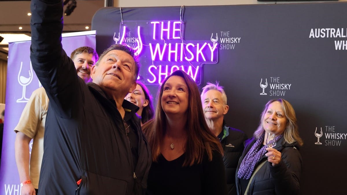 A group of friends gather in front of a Whisky Show banner and Neon Sign.
