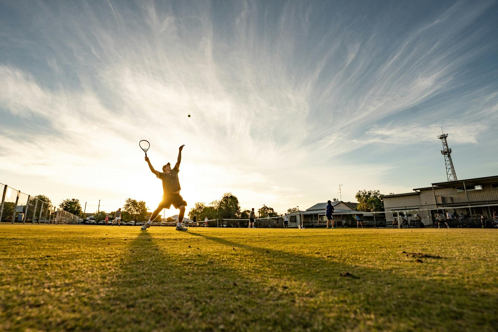 The silhouette of a tennis player serving casts long shadows