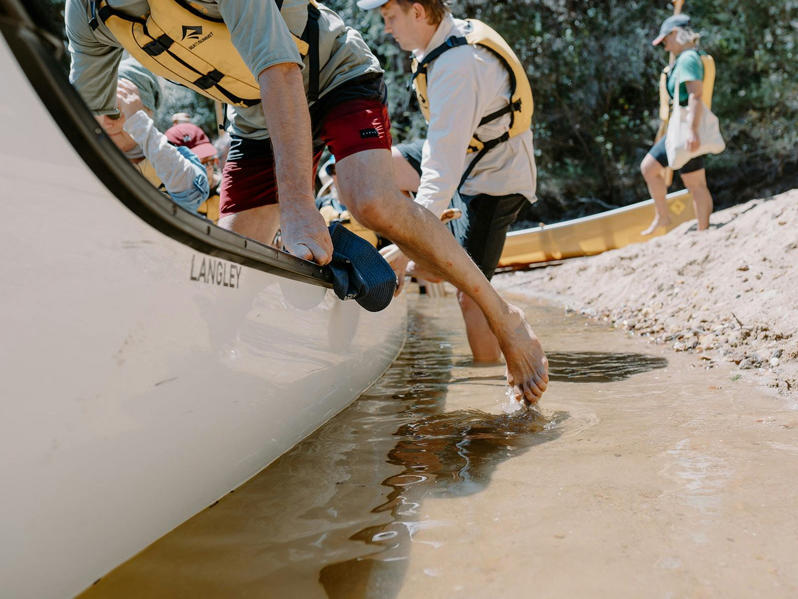People stepping from the water  into a large white canoe on a sunny day