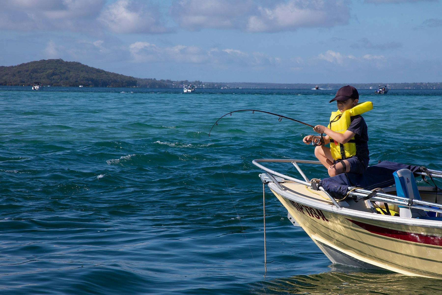 Child in lifejacket fishing off boat