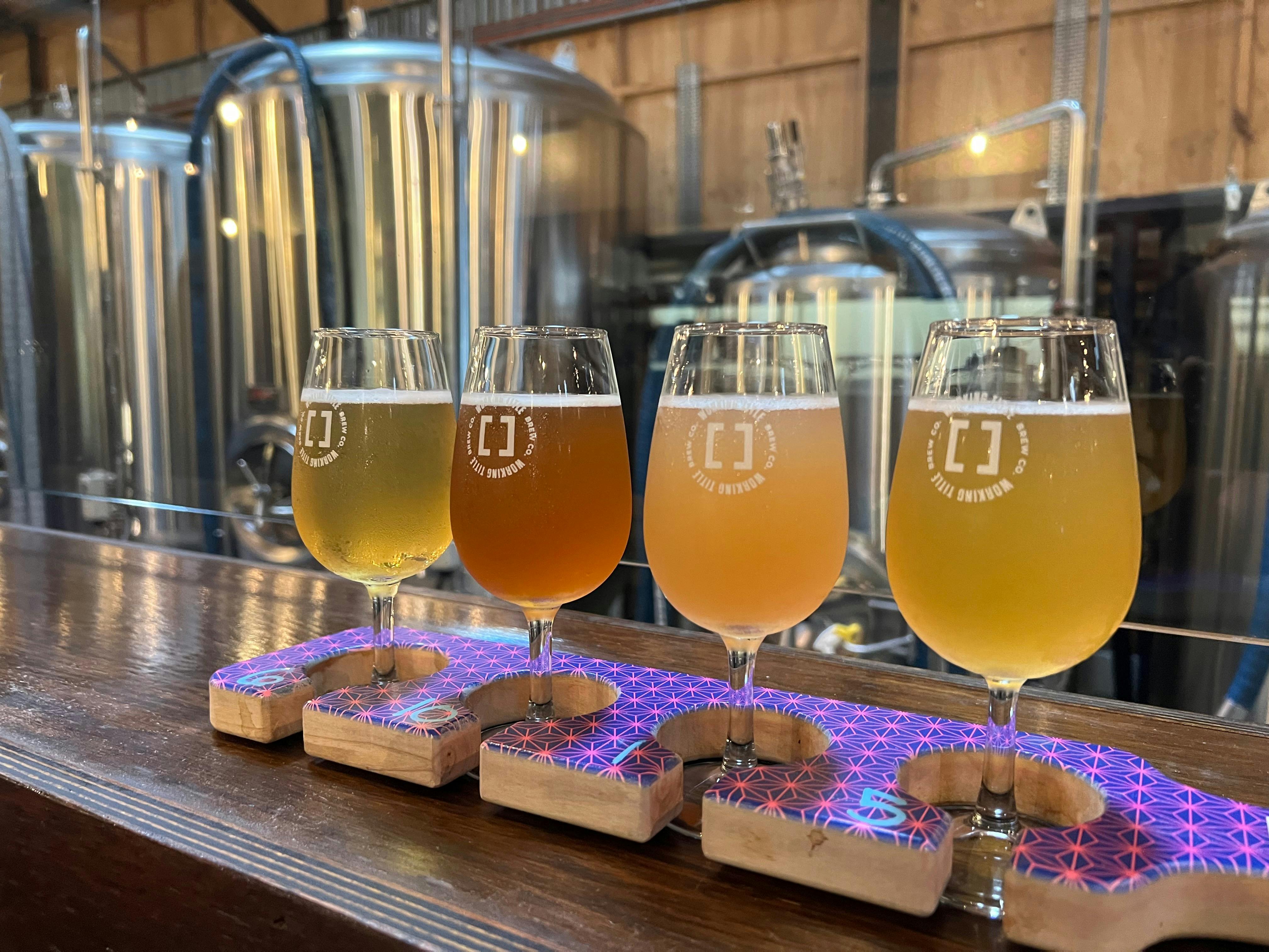 - Four beers on a tasting paddle in front of steel beer vats at Working Title Brew Company
