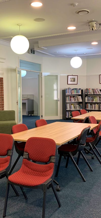 Image of large reading room with table and chairs, book shelves and round suspended lights