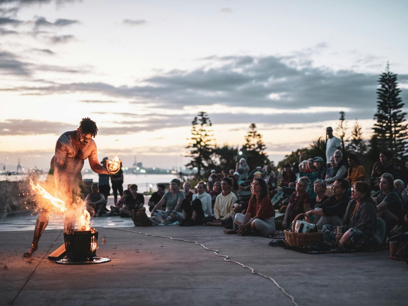 A First Nations performer lights a fire as a crowd watches on at sunrise. A First Nations performer lights a fire as a crowd watches on at sunrise.