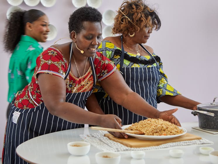 Two African women lean over their food preparation, laughing