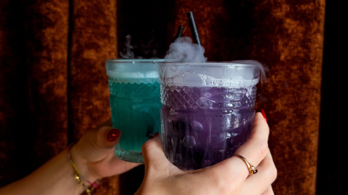 two cocktails held up against an orange curtain