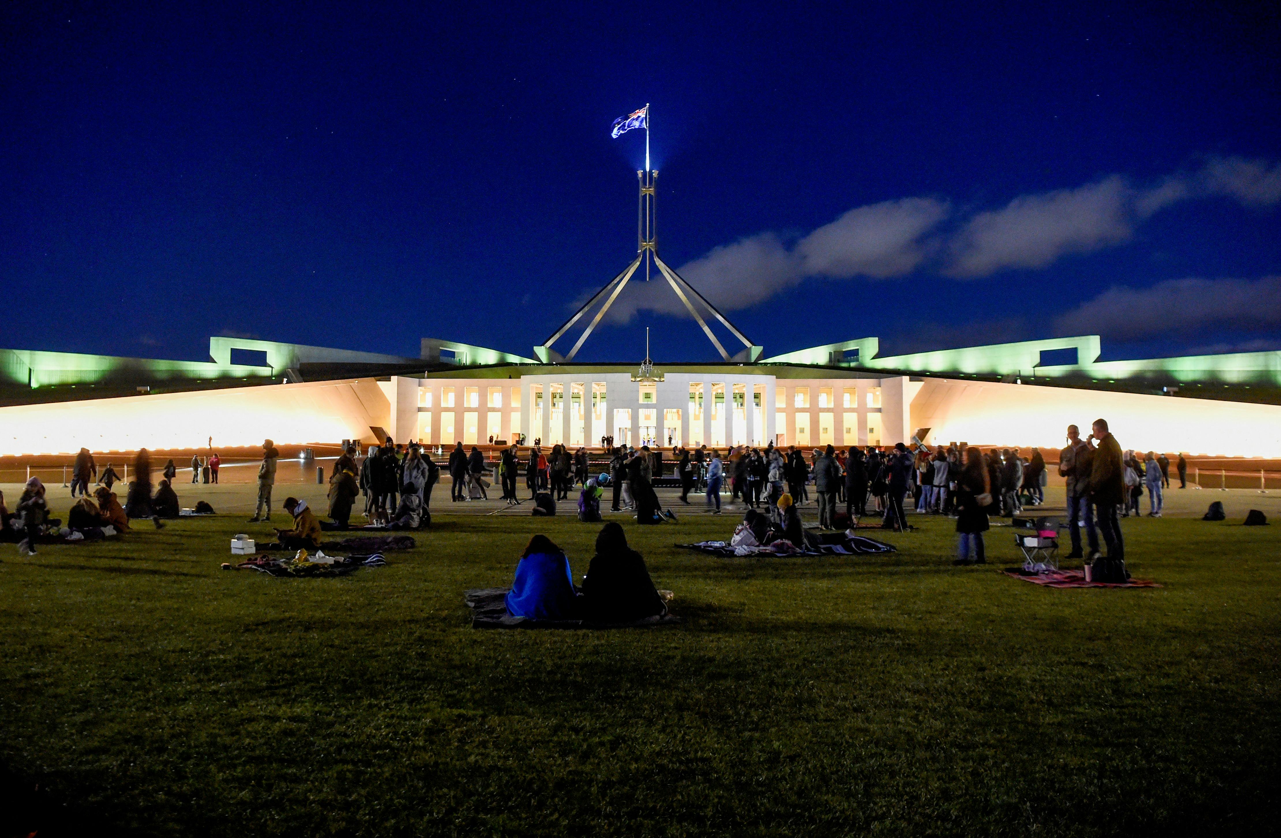 People sitting on the lawn of Parliament House at night.