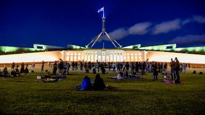 People sitting on the lawn of Parliament House at night.