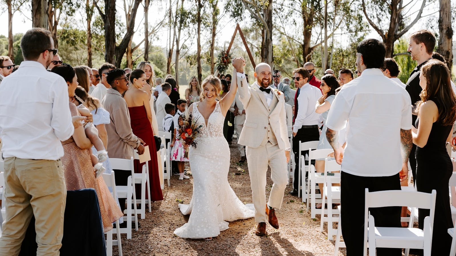 Bride and groom walking down aisle at Eight Acres ceremony space under gum trees, guests cheering