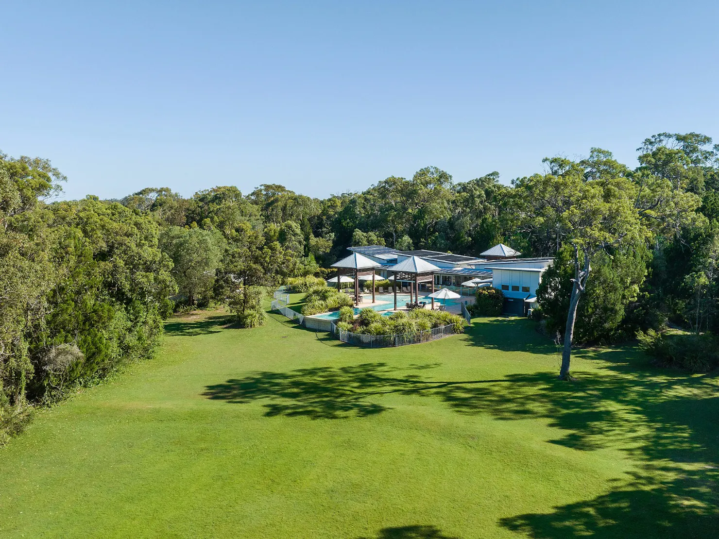 Aerial view of the leisure centre, large village green, pool, and surrounding bushland.