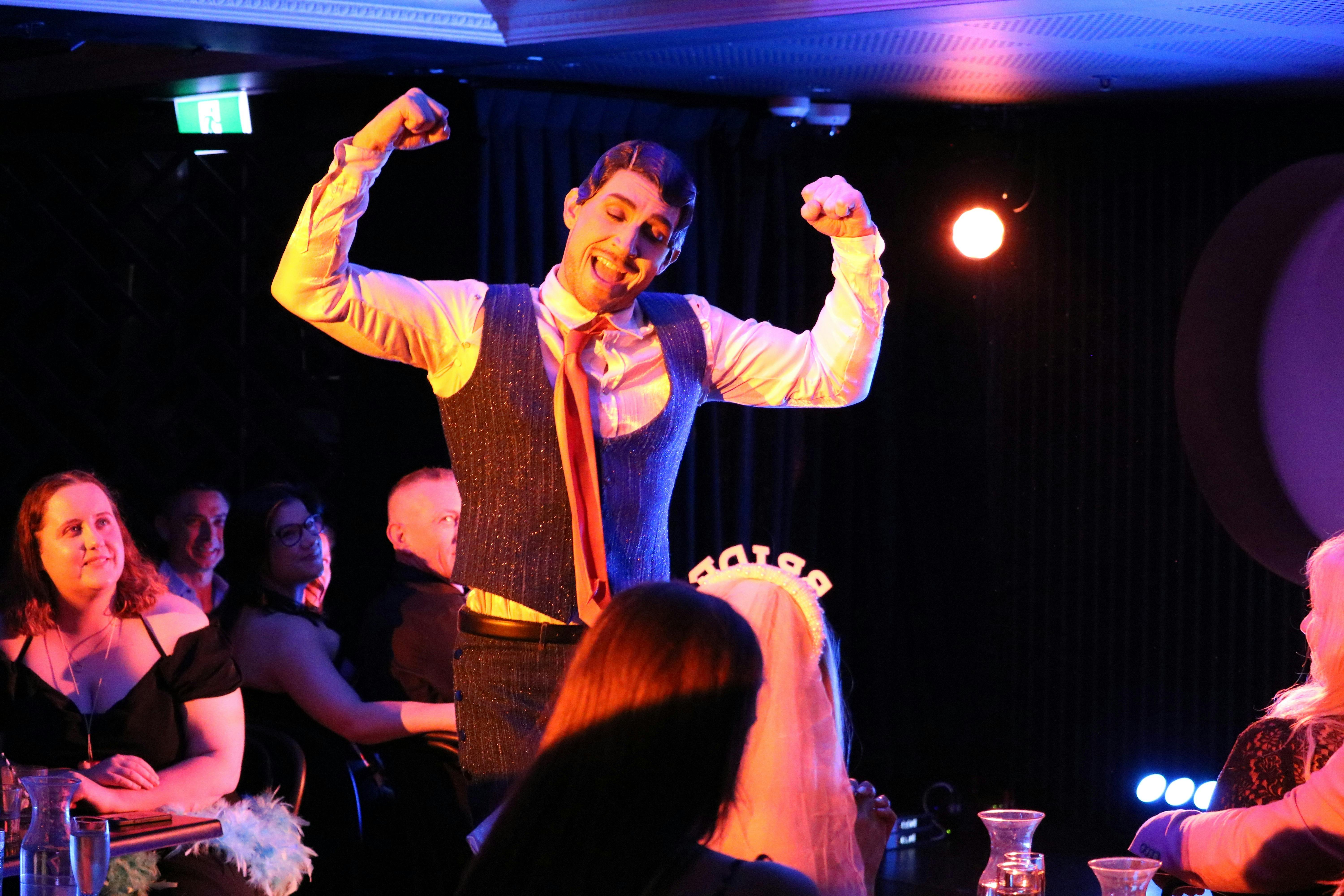 Rhys Lightning strikes a pose with two arms flexing, wearing a vintage suit.