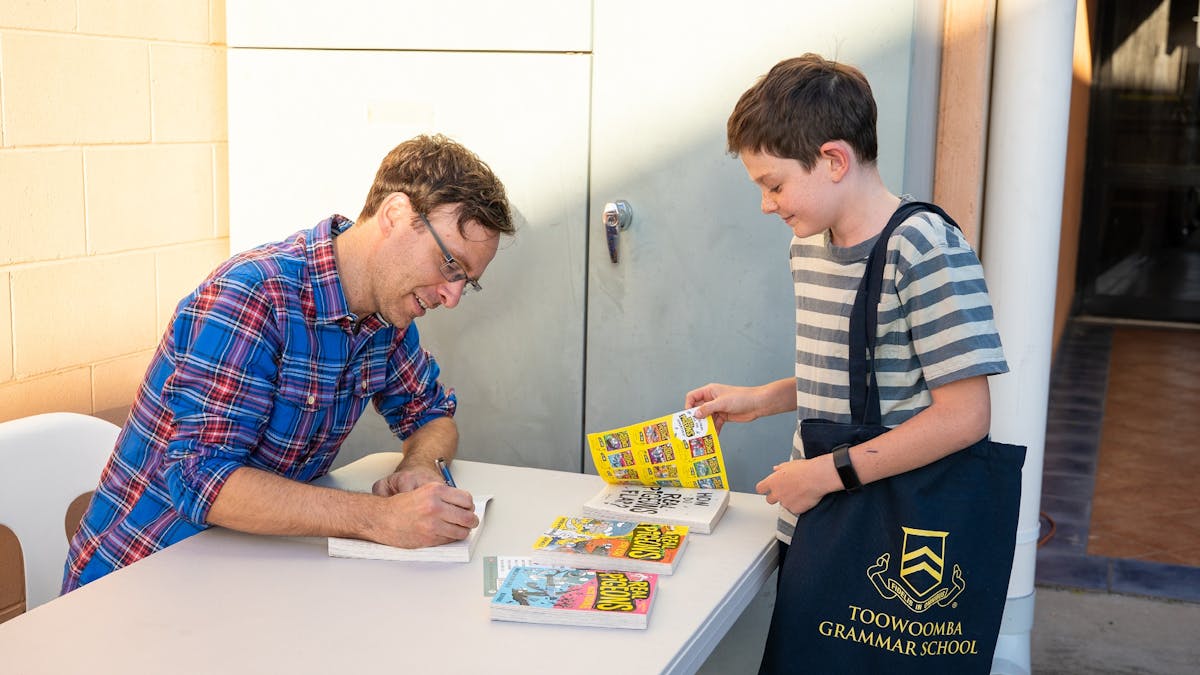 Author signs books for a student at a Storyfest school event.