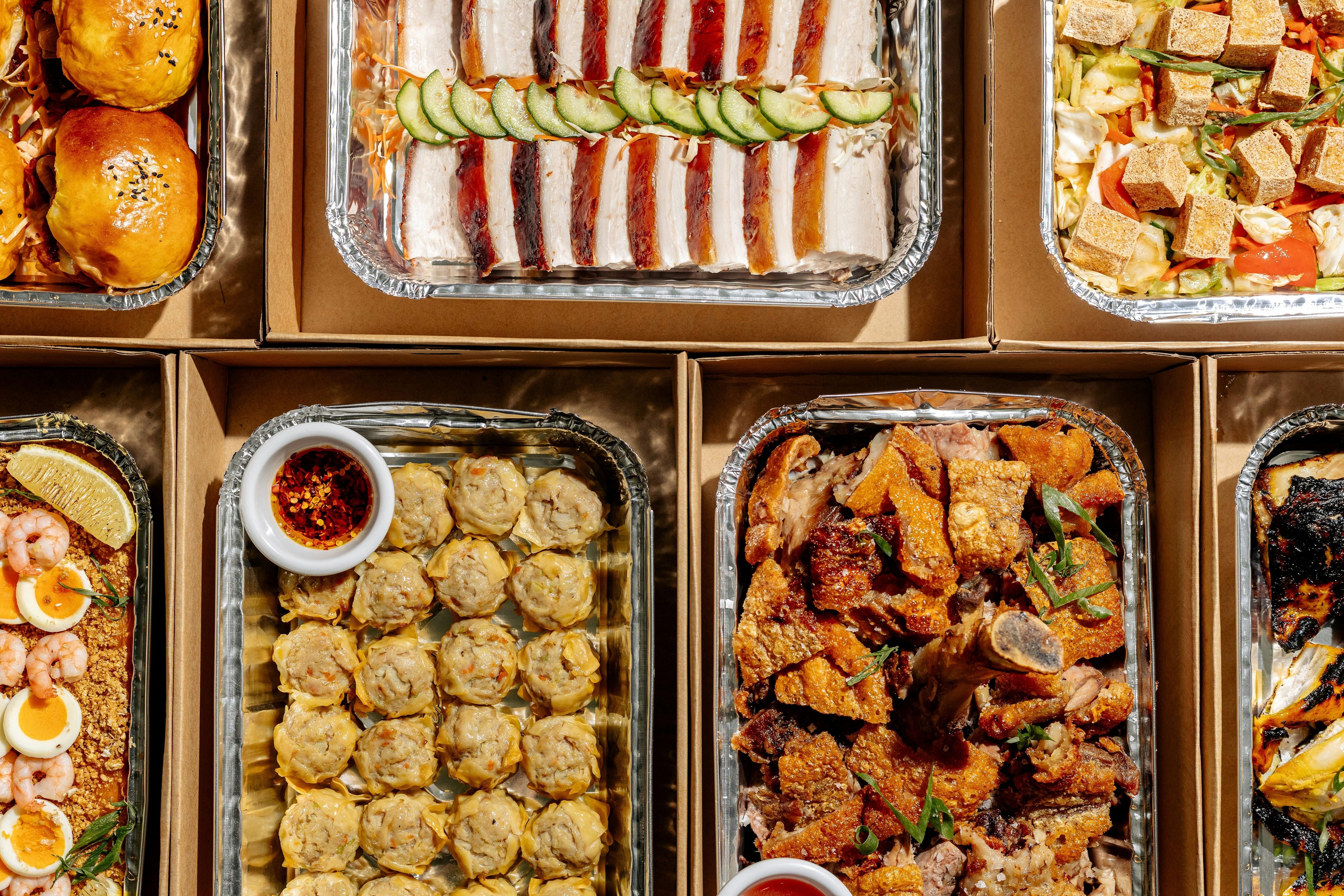 Assorted Filipino catering trays filled with roasted meats, buns, dumplings, seafood, salads and veg