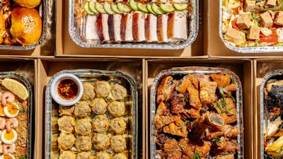 Assorted Filipino catering trays filled with roasted meats, buns, dumplings, seafood, salads and veg