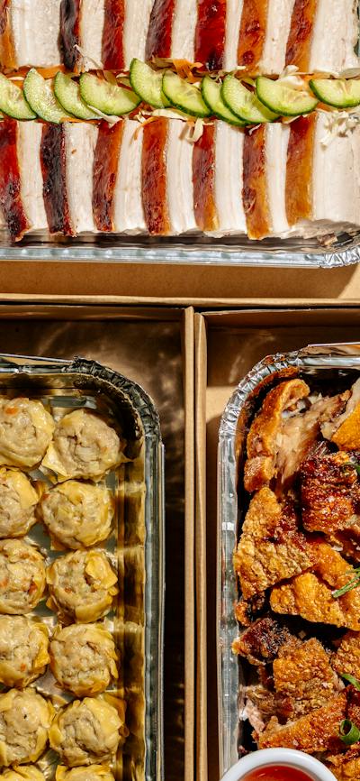Assorted Filipino catering trays filled with roasted meats, buns, dumplings, seafood, salads and veg