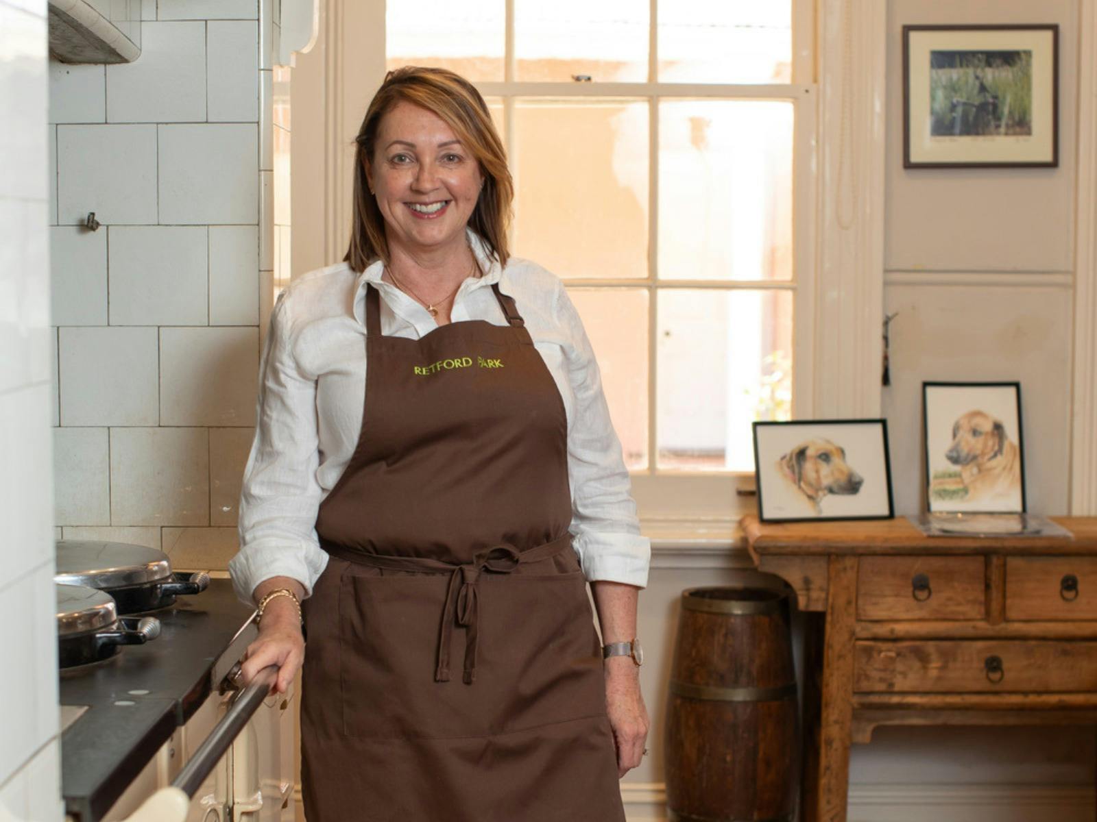 Lady wearing an apron stands in the kitchen. Family photos are positioned in the background.
