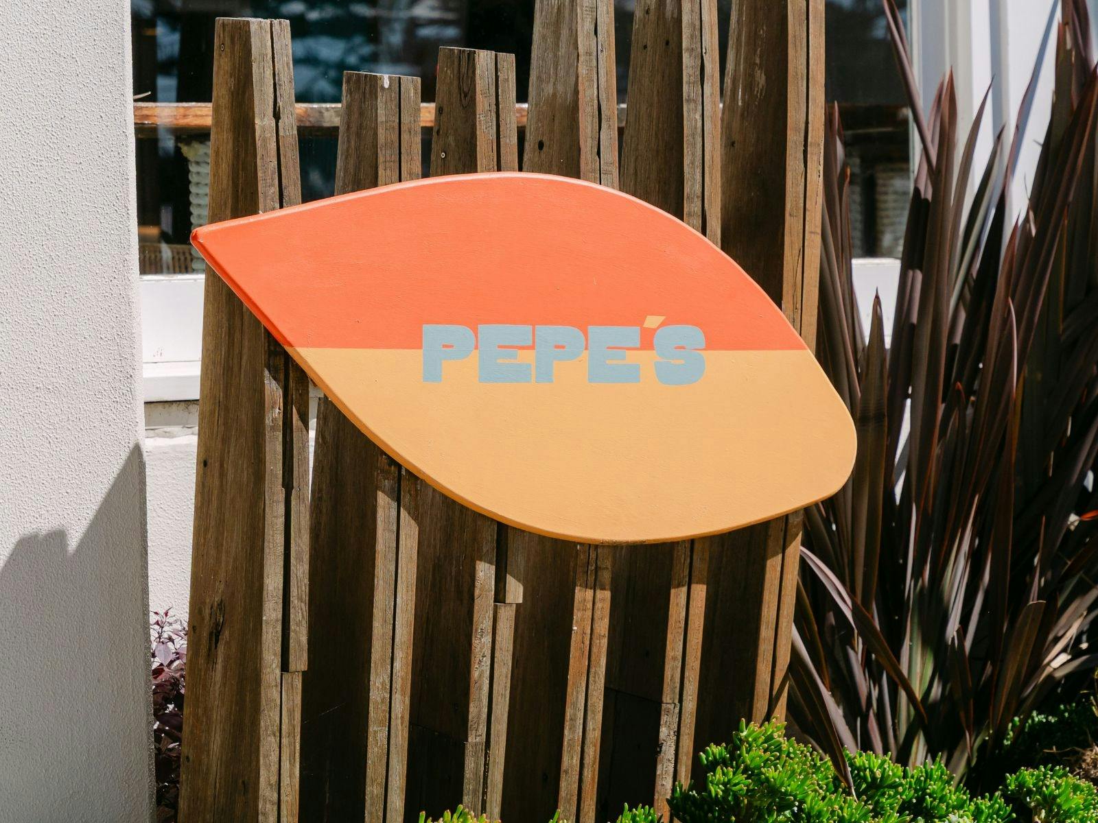 Pepe’s on the Beach surfboard-style venue sign displayed beside the outdoor deck.
