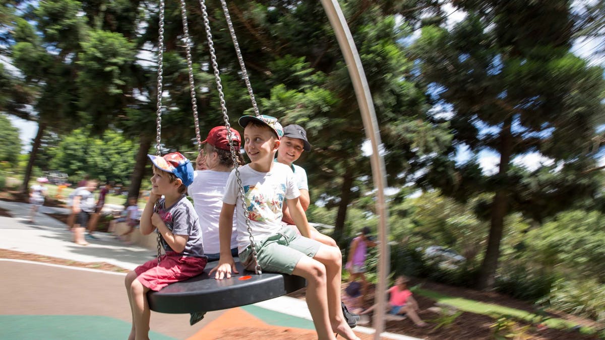 Four kids sitting on a large round swing at Pine Rivers Park