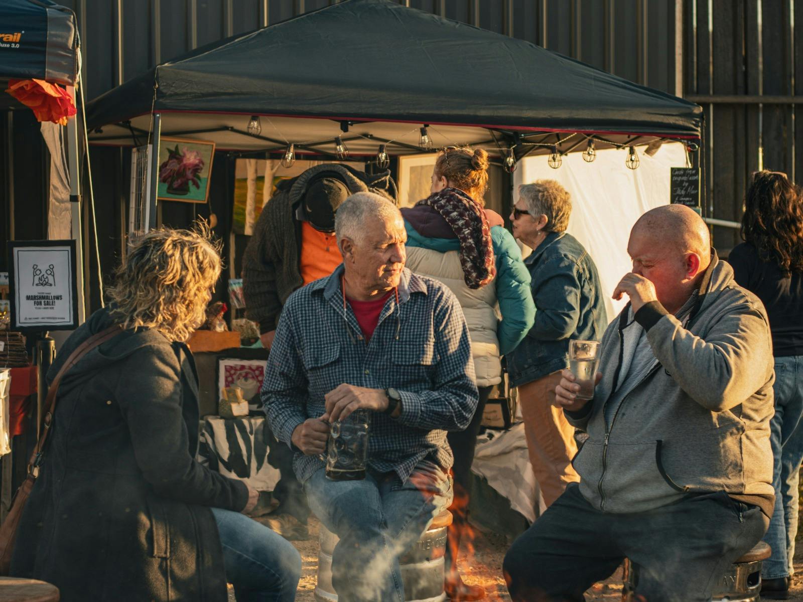 Visitors seated by a fire near an artisan stall at Easy Tiger, St Helens.