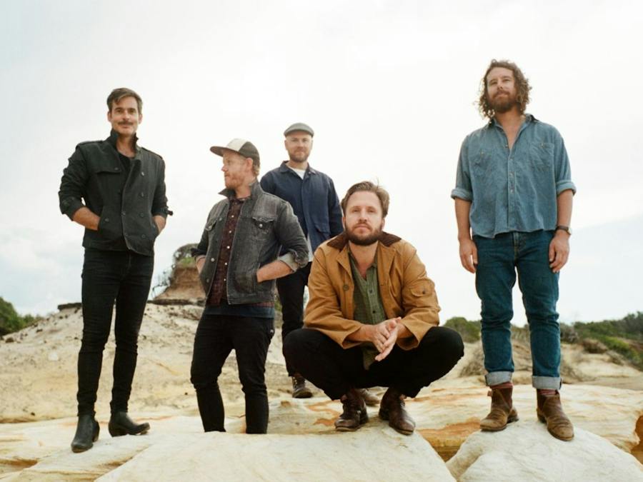 five band members all make standing on rocks looking out to sea