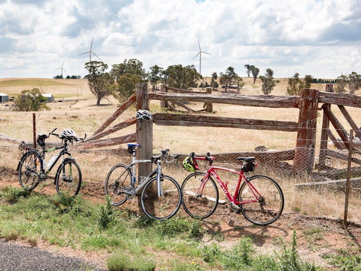 Three bicycles lean up against a wire fence beside an old timber cattle yard.