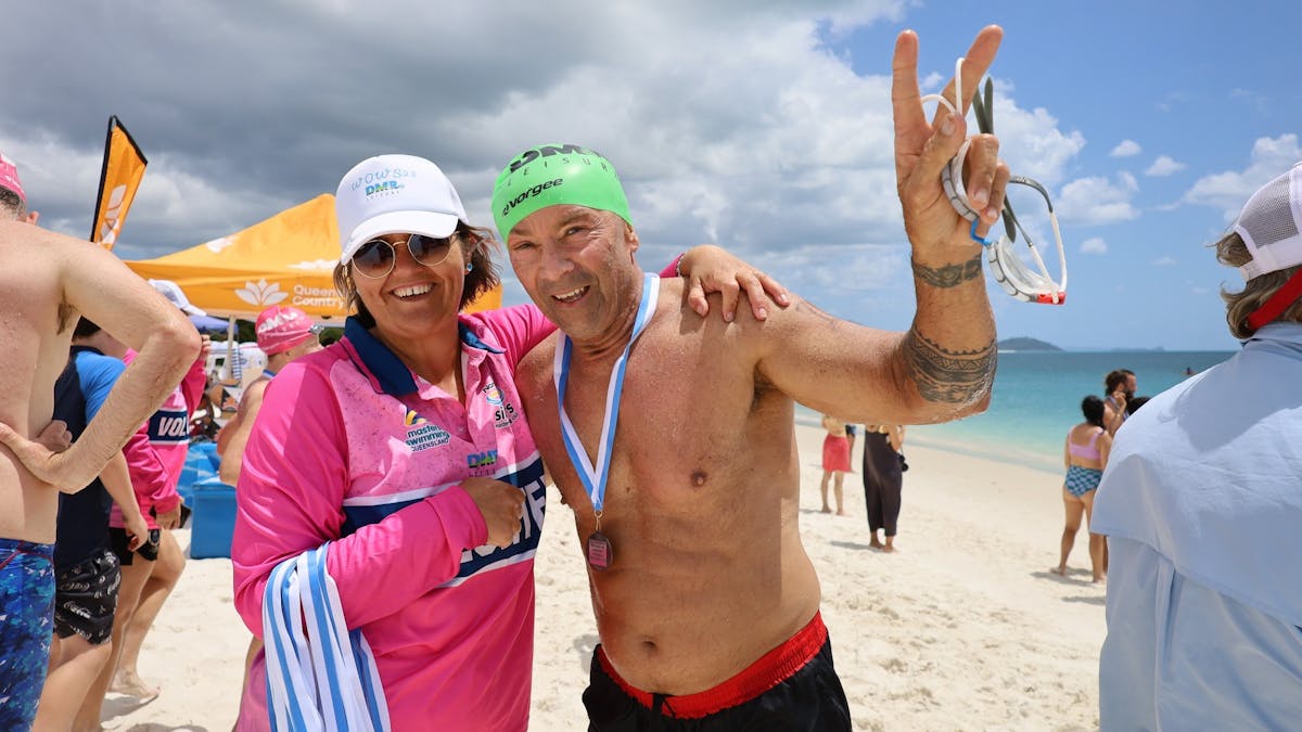 swimmer with arm around finish line volunteer smiling after getting presented with medal
