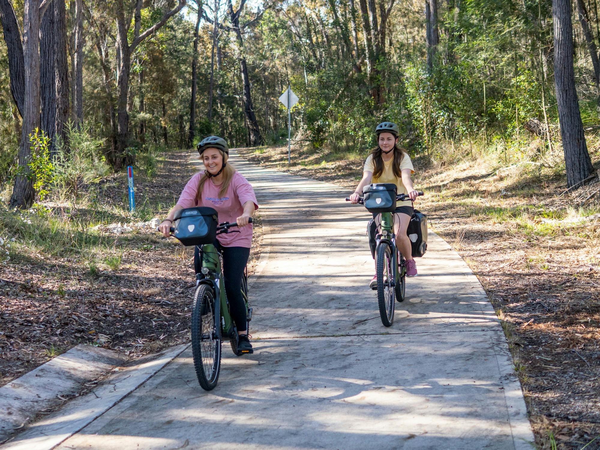 Two guests cycling along a bike path with bush in the back ground
