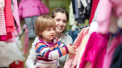 A small boy with a women touching clothes hanging on a rack at a market stall