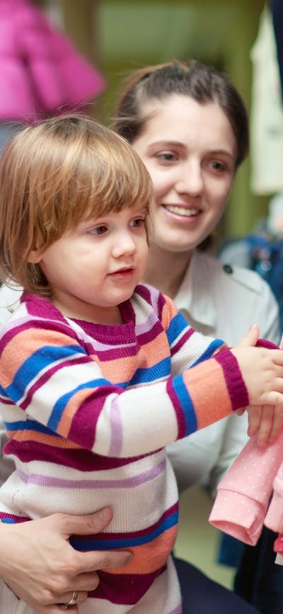 A small boy with a women touching clothes hanging on a rack at a market stall