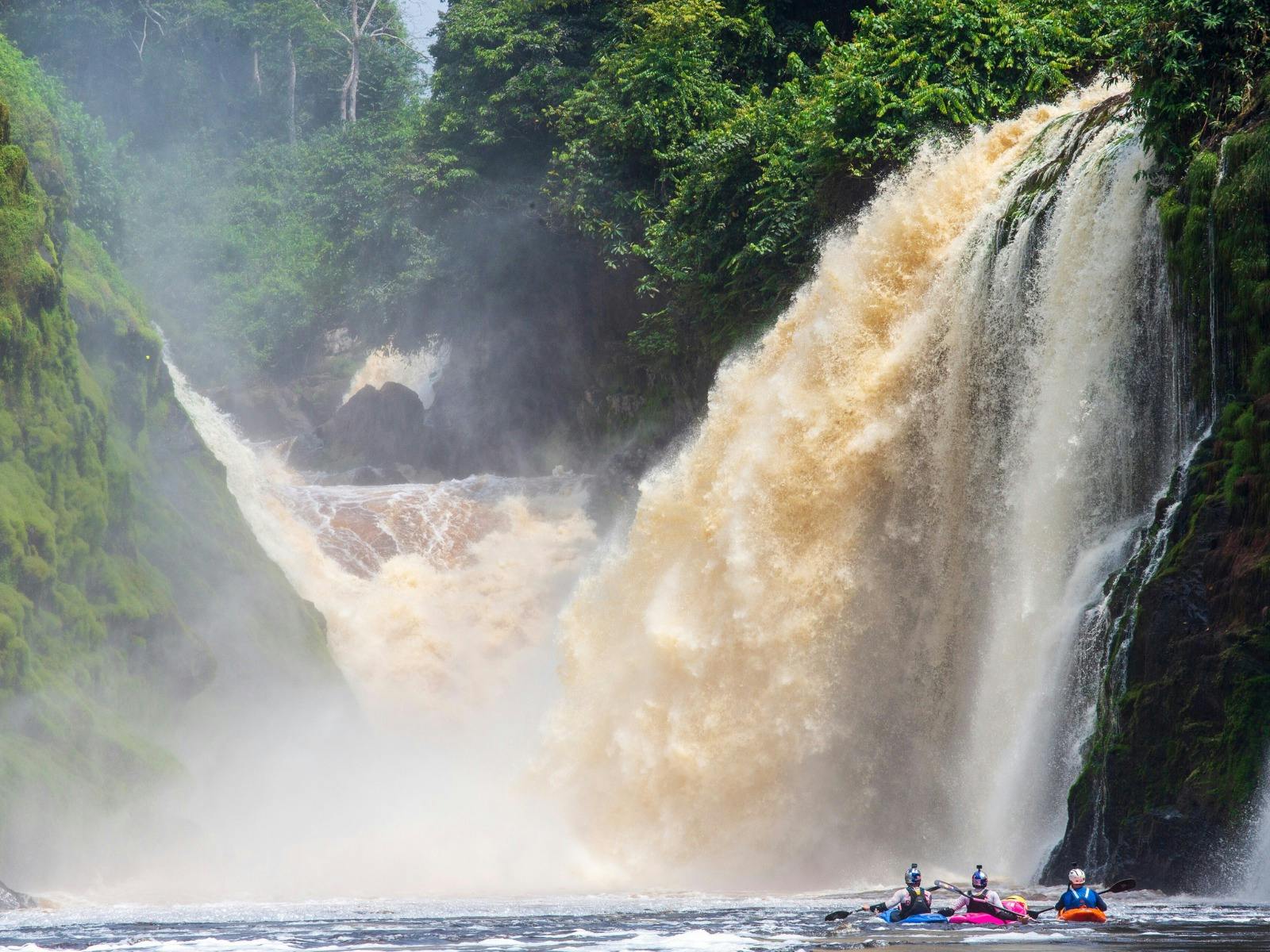 Kayakers under a large waterfall