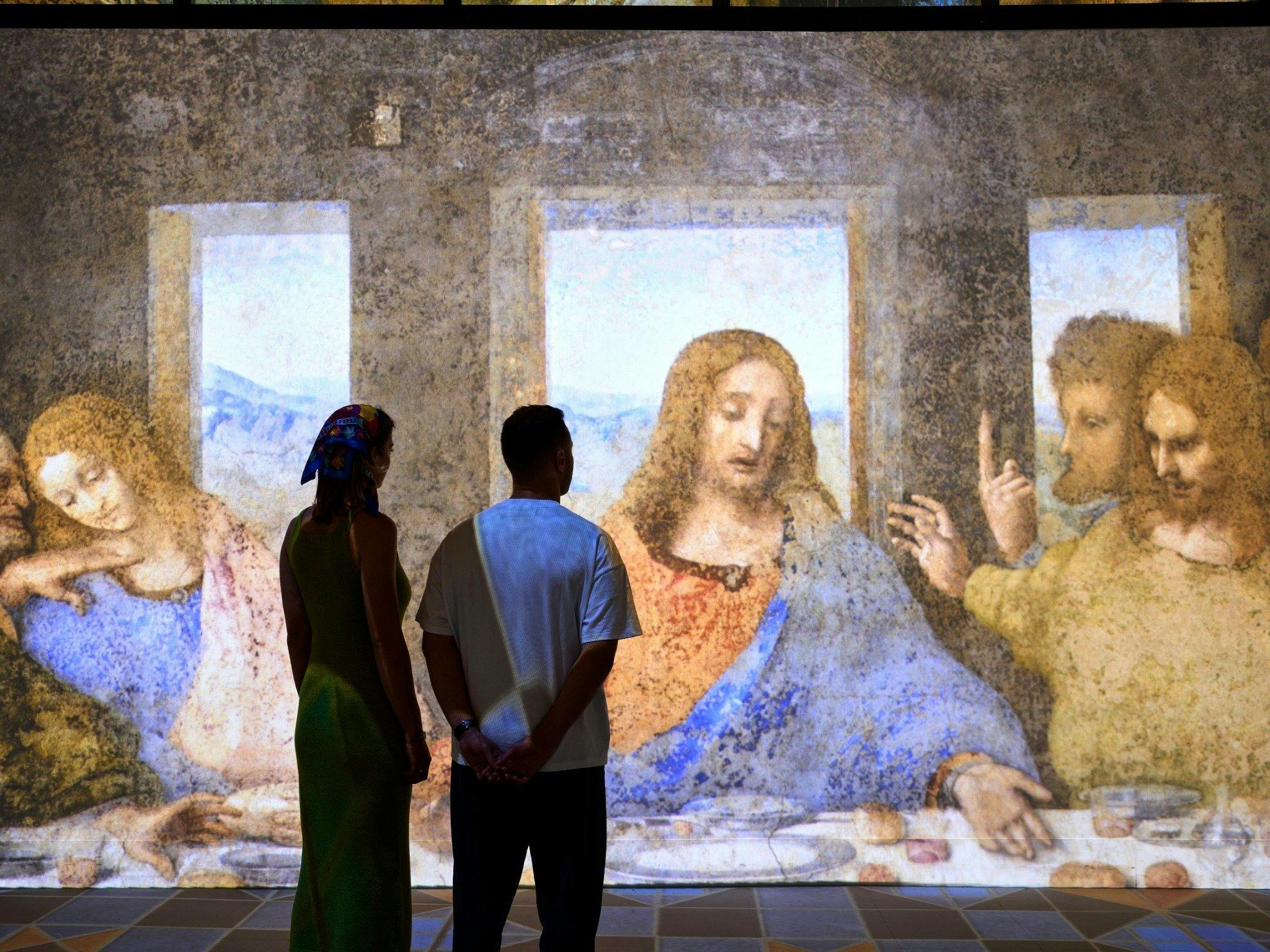 Visitors stand before a large immersive projection of The Last Supper in a gallery space.