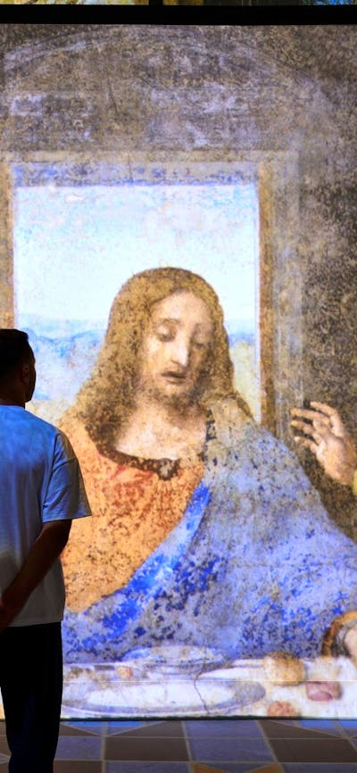Visitors stand before a large immersive projection of The Last Supper in a gallery space.