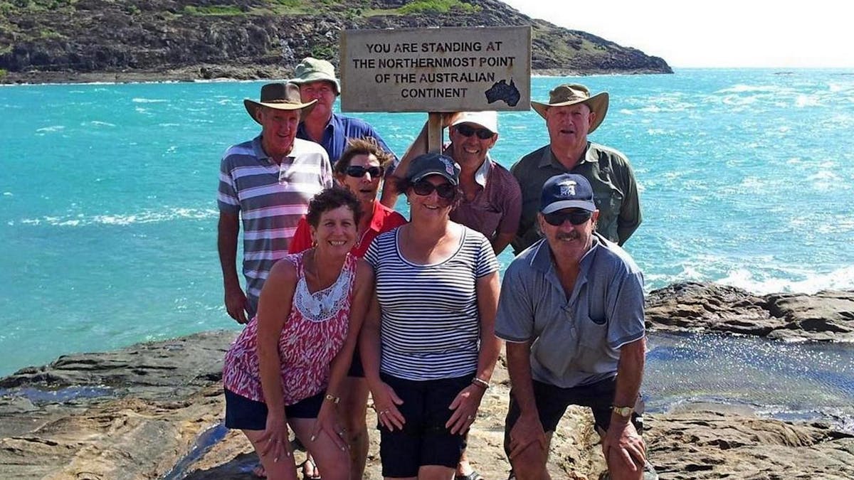 Tour group posing for photos by the sign at the tip of Cape York with York Island in the background.