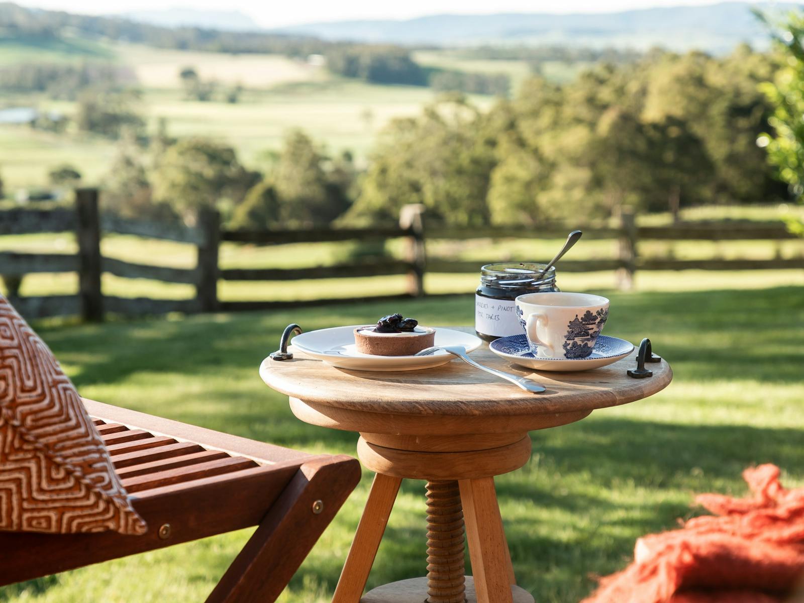 Table with tea, tarts and a jar of pinot soaked cherries sits on a deck overlooking a green valley