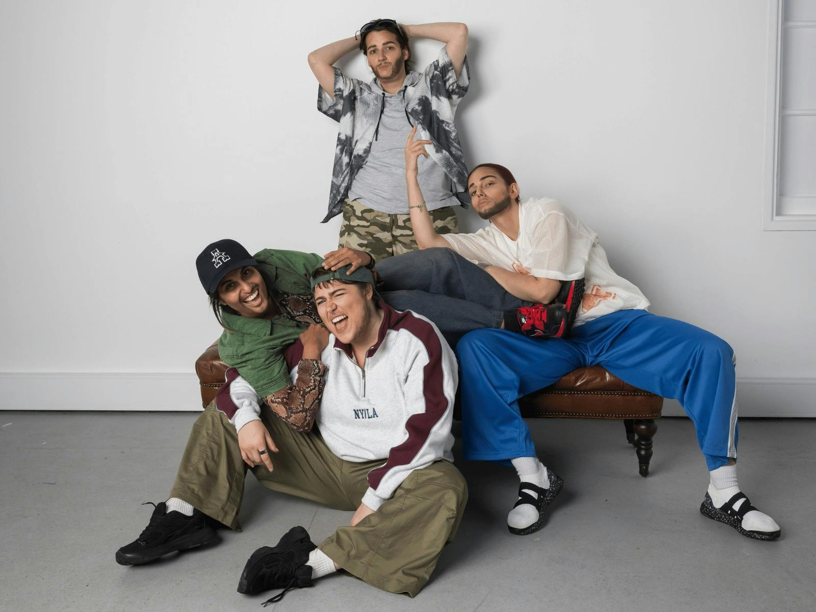 Four Drag Kings dressed as boy band members posing on and around a brown leather chair