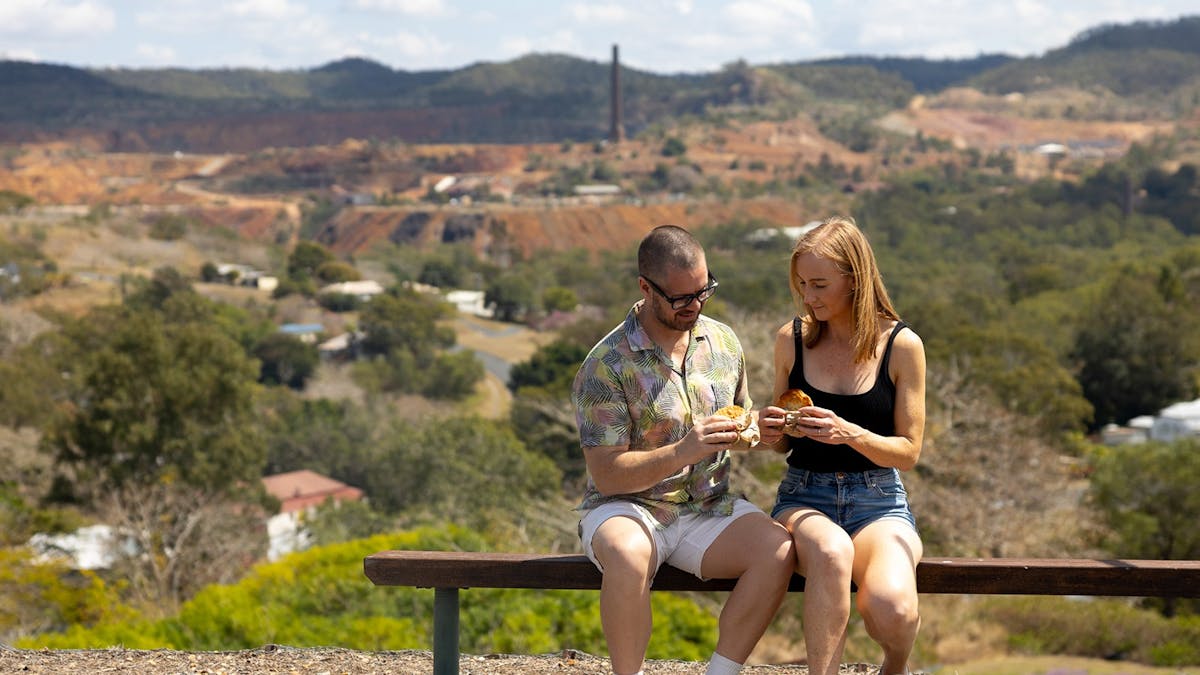 Young man and woman enjoying a meat pie at a lookout at Mount Morgan