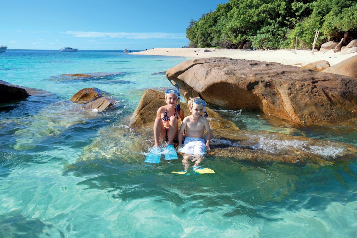 Children in snorkelling gear on boulder at beach at Fitzroy Island