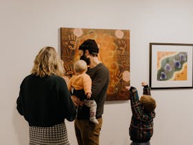 A family look at Aboriginal artwork on a wall, their backs are to the camera.
