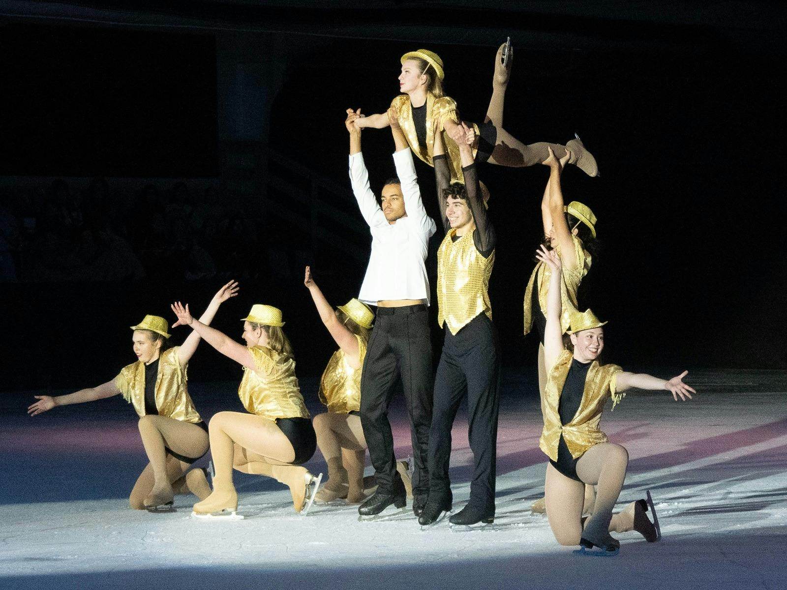 Figure skaters in Gold, Black and white, lifting one skater