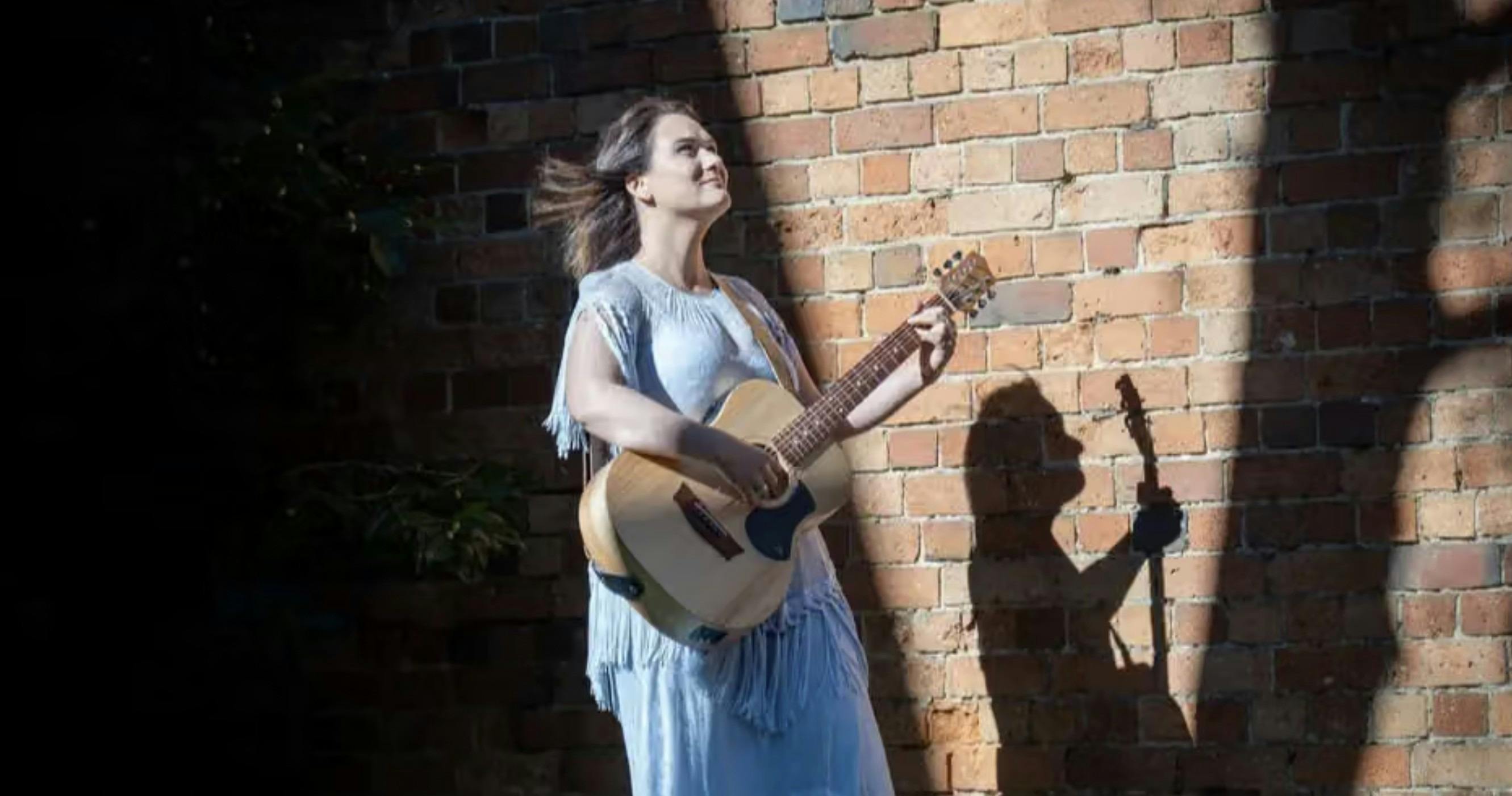 Woman in blue dress singing with guitar