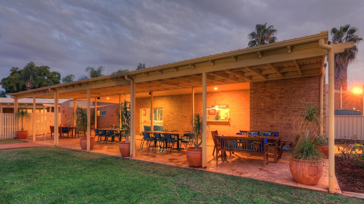 Evening photo showing lawn and undercover seating area with 4 tables and chairs