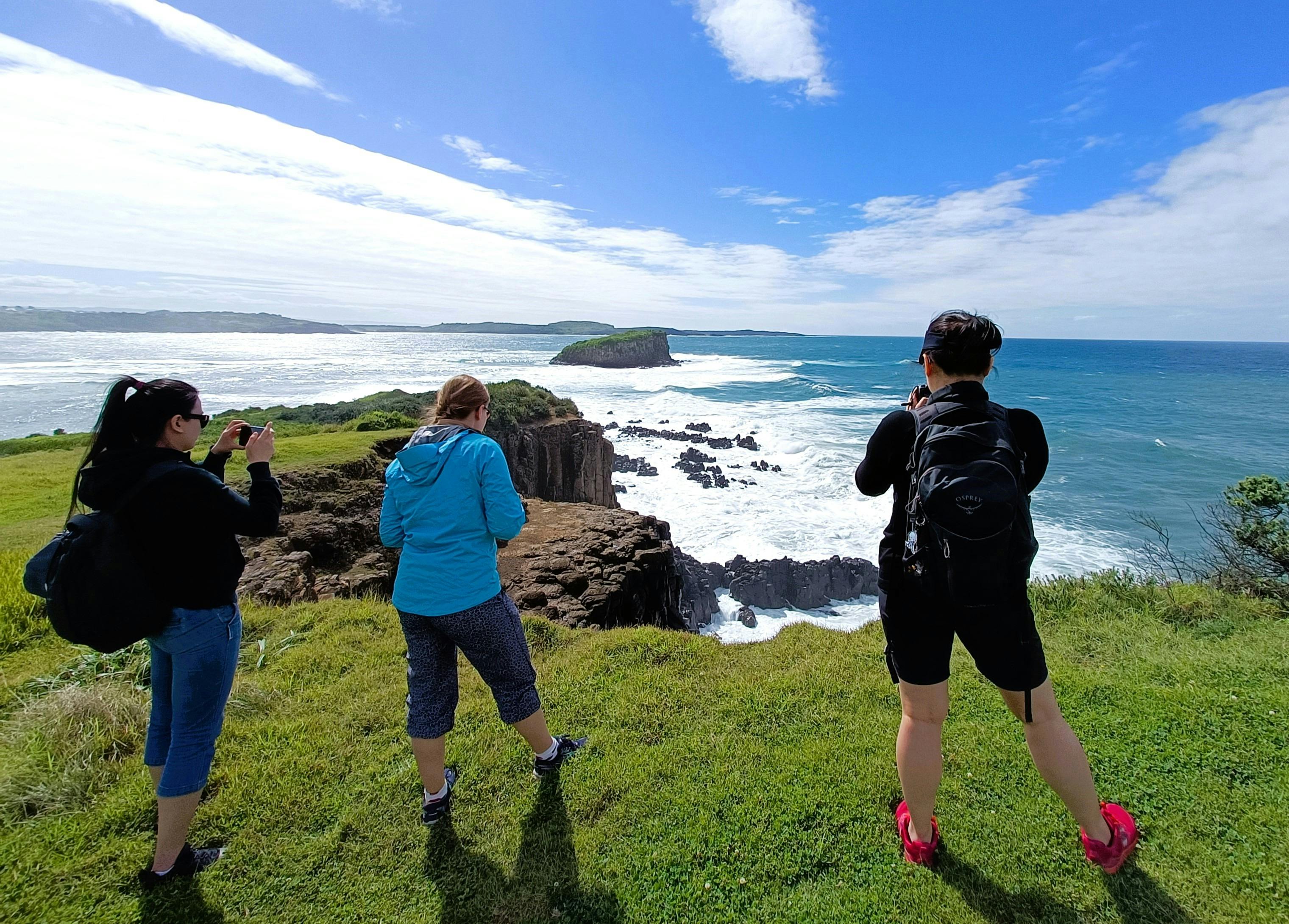 three women taking photos of dramatic coastal cliff views