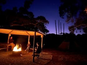 Please sitting around a campfire within campfire circle under shelter and night sky