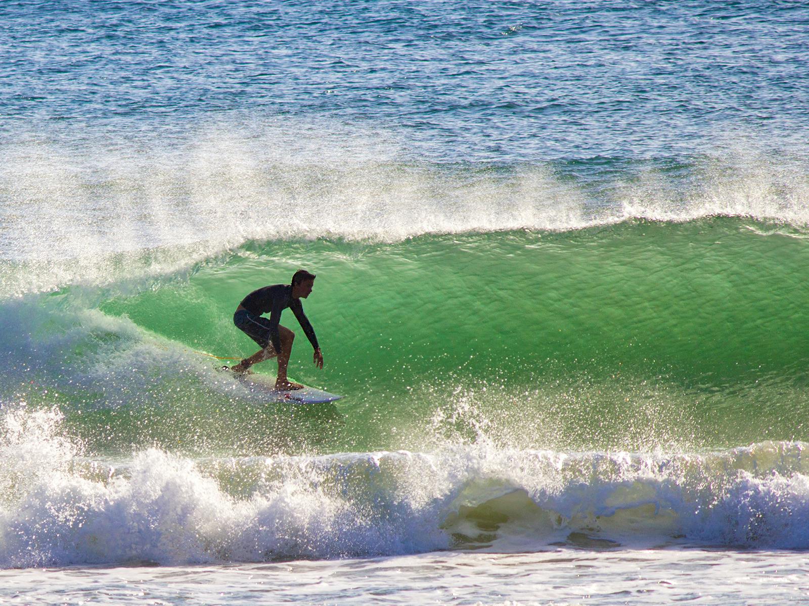 Silhouette of a surfer as he rides the wave, while the onshore wind sprays the foam
