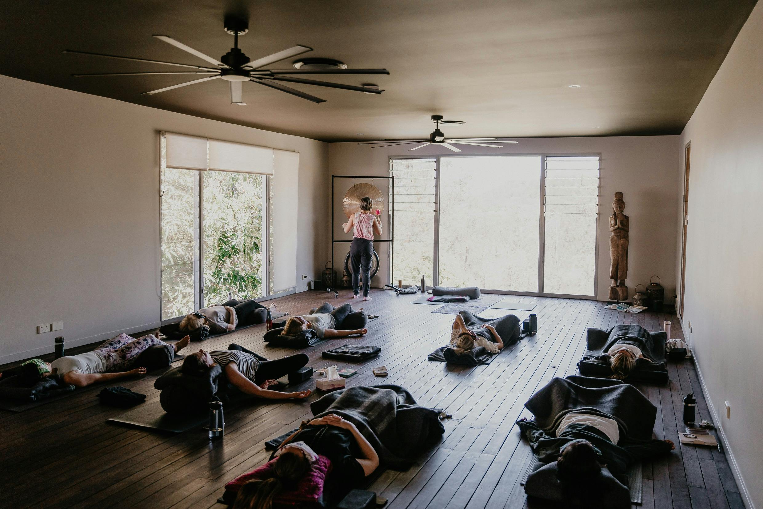 A sound healer leads a gong bath in a retreat room, with guests lying  together as they experience t