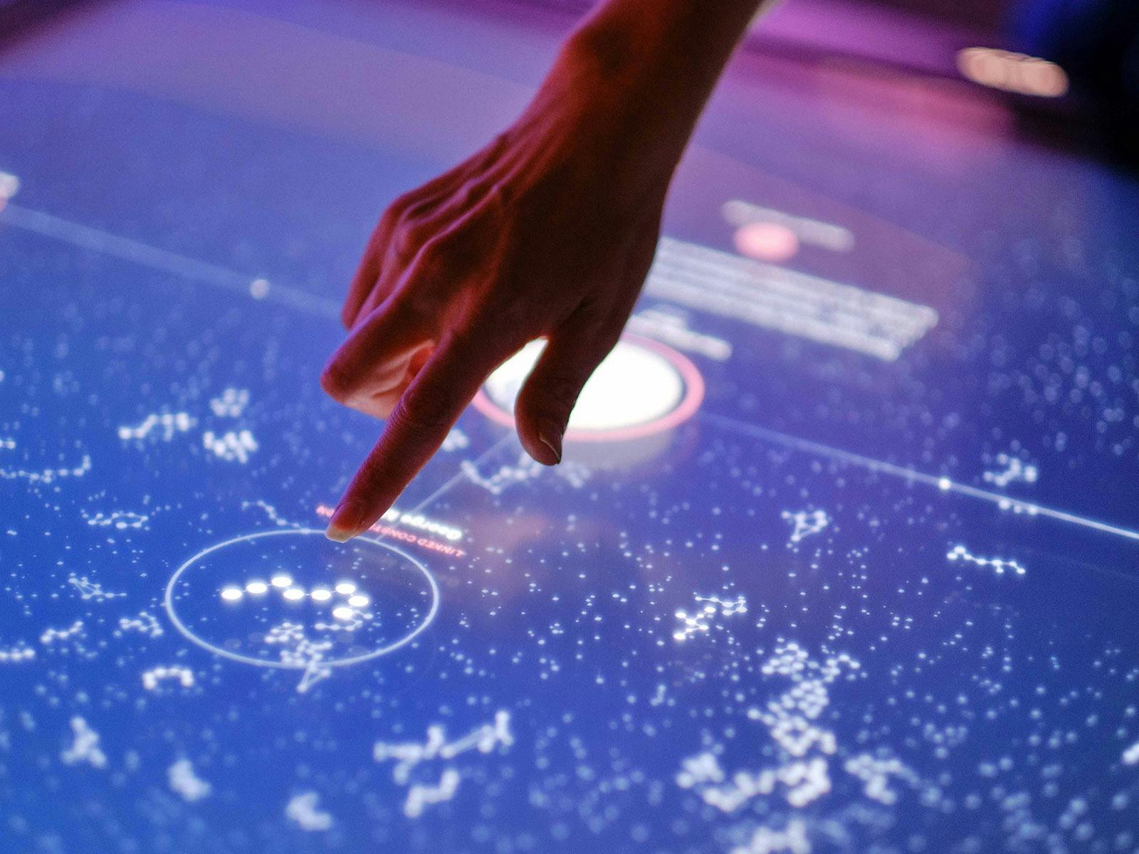 A hand points at a screen, lighting up with constellations