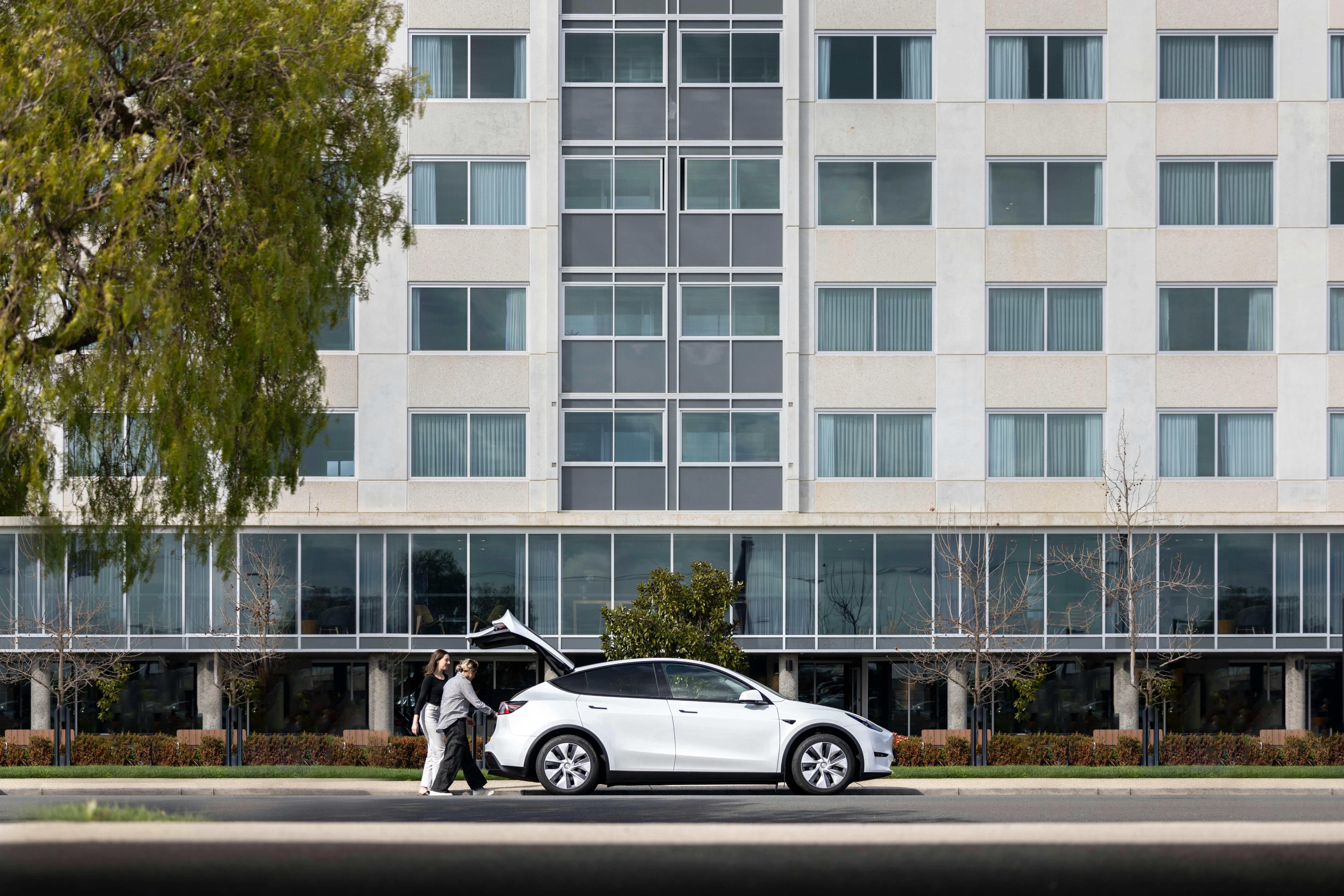 EV hire (Tesla Model Y) parked in front of a hotel in with tourists unloading luggage from the trunk